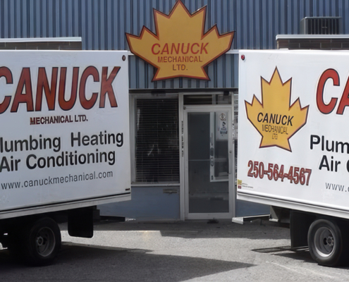 CANUCK Plumbing Heating Air Conditioning trucks with a maple leaf logo parked by the company’s blue BC HVAC service building.