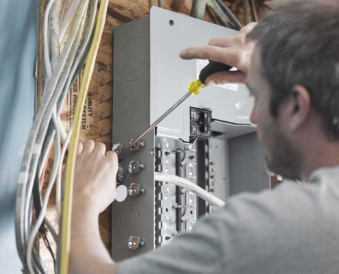 Technician repairs wiring in electrical panels, surrounded by cables on a wooden wall—expert HVAC service in British Columbia.