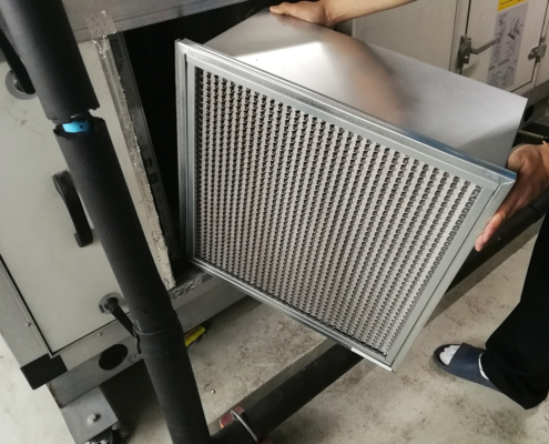 A person in socks changes a large metal-framed air filter in an industrial HVAC unit, common for BC HVAC maintenance services.