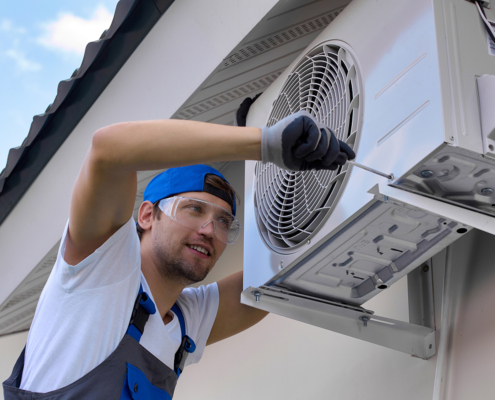 HVAC technician in safety gear repairs an outdoor heat pump unit mounted on a building wall in British Columbia.