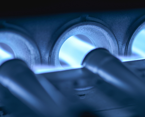 Close-up of blue flames in a gas furnace with three glowing burner tubes, highlighting efficient heating for British Columbia homes.