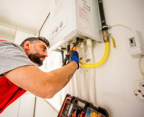 HVAC technician in British Columbia repairs a wall-mounted gas boiler with tools, pipes, and wires visible in the background.