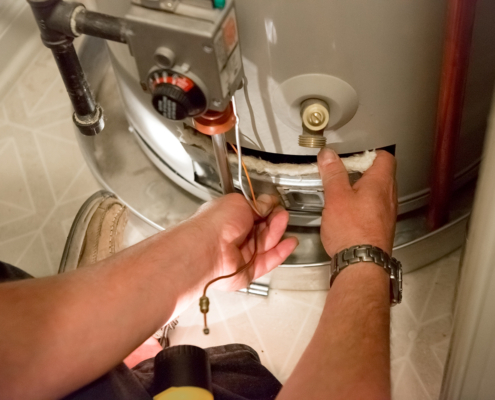Technician repairing a water heater’s lower section with tools, insulation, and pipes visible—HVAC maintenance in British Columbia.