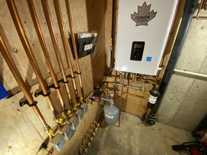 Utility room with copper pipes, valves, a gray expansion tank, and a Canuck Mechanical heating unit on wood wall in BC.
