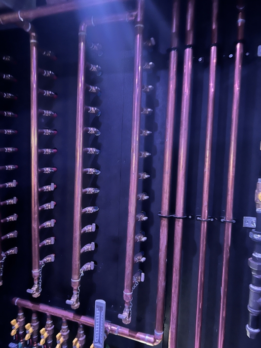Vertically mounted copper pipes with valves and fittings on a black wall, showcasing HVAC plumbing installation in British Columbia.