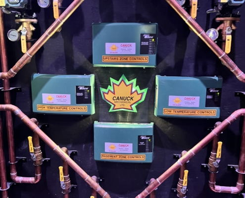 Copper pipes and green “Canuck” control boxes for zoned HVAC in BC, with gauges and valves neatly arranged on the wall.