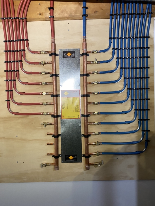 Neatly installed plumbing manifold with red hot water and blue cold water pipes, connected to copper, for HVAC in British Columbia.