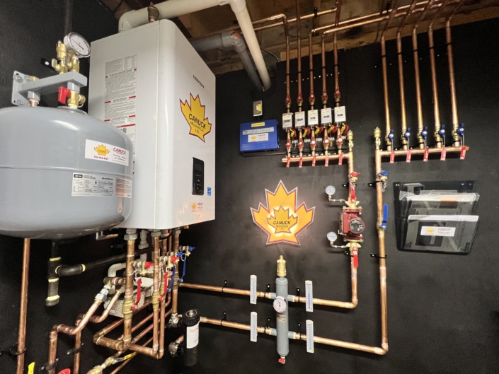 Mechanical room showcasing wall-mounted HVAC system, copper pipes, gauges, expansion tank, and CANUCK maple leaf stickers in BC.