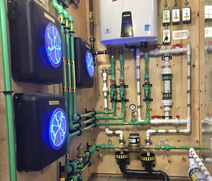 Green and black HVAC pipes, valves, and gauges connect to blue-lit control boxes and a water heater in a BC utility room.