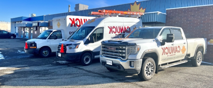 Chanik HVAC service vehicles, including a GMC truck and two vans with equipment, parked at a blue and brick BC business location.